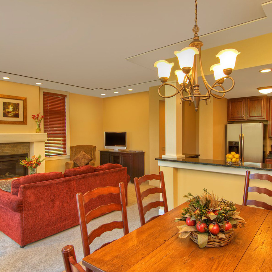 A view of a dining room, living room with sofa and fireplace, and full kitchen with full refrigerator and oven